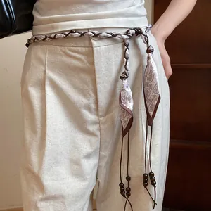 Detailed view of a bohemian silk scarf waist chain with wooden beads on linen pants.