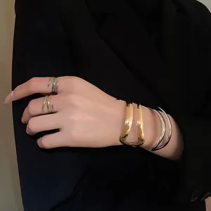 Dettaglio ravvicinato di bracciali aperti geometrici oro e argento e anelli a spirale