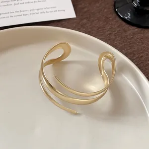 Dettaglio di un bracciale rigido dorato geometrico minimalista con design a strati.