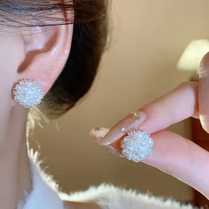 Detailed view of elegant pearl flower cluster stud earrings on ear and hand.