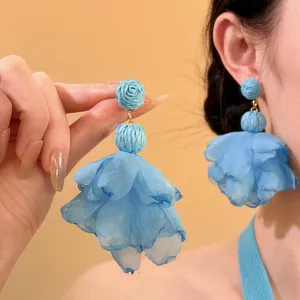 Detail view of blue raffia ball and fabric flower tassel dangle earrings on model