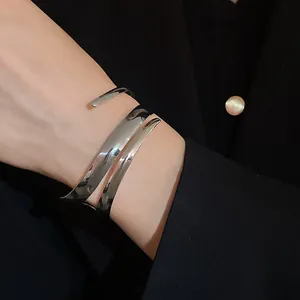 Vista di un bracciale rigido aperto argento geometrico minimalista sul polso di un modello