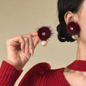 Detail view of deep red fur ball earrings with zircon center and pearl drop worn by model