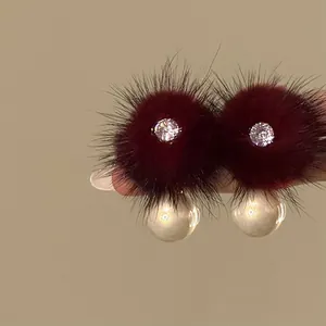 Close-up of burgundy fur pom-pom earrings with zircon and pearl detail