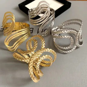 Detail view of four geometric open bangles with hollow wave and rope textures in gold and silver.