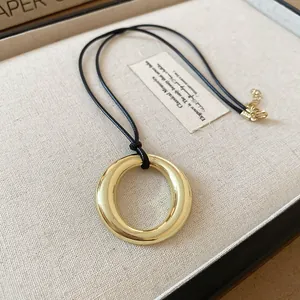 Minimalist gold-colored circular ring pendant necklace with black leather cord