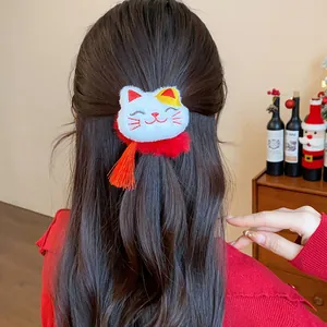 Dettaglio di un elastico per capelli a forma di gatto della fortuna con nappa rossa