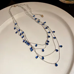 Primer plano de collar multicapa plateado con elegantes circonitas azules en forma de pera.