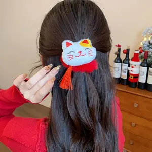 Dettaglio di un elastico festivo in peluche a forma di gatto rosso con nappa sui capelli