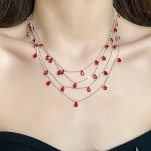 Vista detallada de un collar multicapa de circonita con colgantes en forma de gota roja.