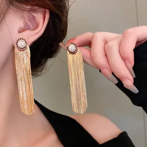 Detailed shot of elegant long gold tassel earrings with pearl and black stone stud