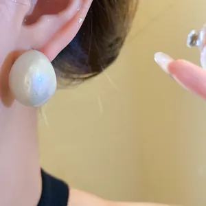 Close-up detail of an oversized acrylic droplet earring featuring a glossy pearl finish on an ear.