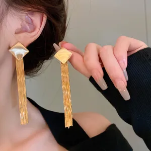 Detail view of gold long metal tassel earrings with square stud on model's ear