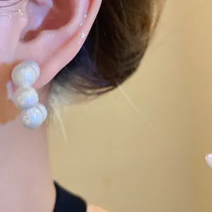Close-up detail view of a stylish minimalist white pearl hoop earring worn on a model's ear.