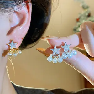 Detail view of star-shaped zircon stud earrings with dangling pearls in gold and silver finish