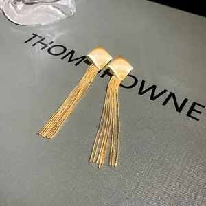 Close-up of elegant gold long tassel earrings with square studs on a grey display