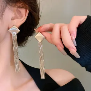 Detail view of long silver metallic tassel earrings with geometric square stud on model