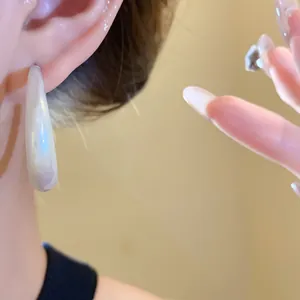 Close-up detail of pearlescent acrylic teardrop earring with elegant rainbow sheen finish