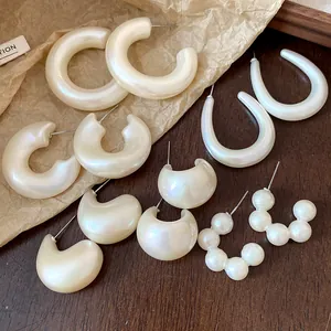 Detailed macro view of various pearly acrylic hoop and stud earrings on vintage paper.