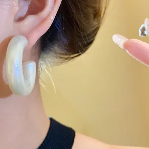 Detail close-up of iridescent pearly white acrylic C-shaped hoop earring worn on ear