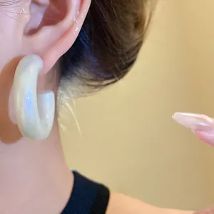 Detail close-up of iridescent chunky pearly white acrylic C-shaped hoop earrings on model ear