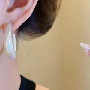 Detailed macro view of elegant white iridescent acrylic C-shape hoop earring on model ear