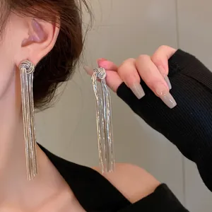 Close-up of elegant long silver metal tassel earrings with a woven knot detail worn on ear