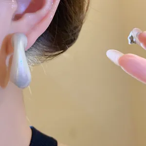 Close-up detail of minimalist pearlescent acrylic teardrop earrings worn on a person's ear