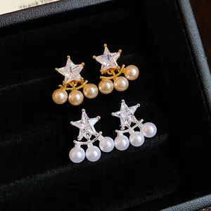 Macro view of elegant star-shaped zircon earrings with dangling pearls in gold and silver