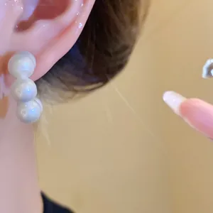 Close-up of acrylic triple-pearl stud earrings worn on the ear, showing fine detail.