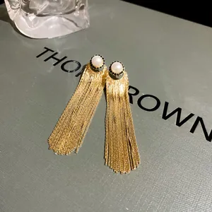 Detailed view of long gold-tone tassel earrings with elegant pearl studs