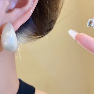 Detailed macro view showing an elegant pearlescent white teardrop earring worn on the ear