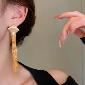 Close-up detail of long gold metal tassel earrings worn by a model in a lifestyle setting