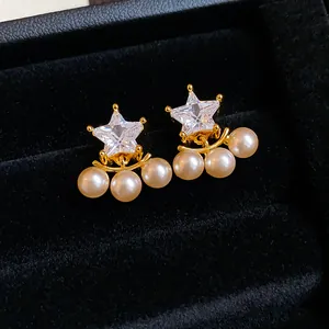 Macro detail of star-shaped zircon earrings with dangling white pearls in a black box.