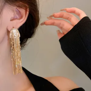 Close-up of gold metal tassel earrings with long drop chains and silver needles.