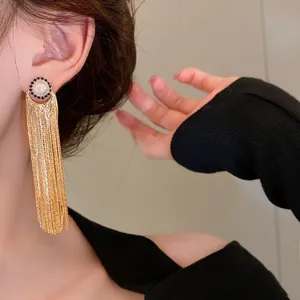 Detailed view of elegant gold metal tassel earrings with pearl and black stone on model