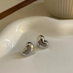 Orecchini a perno a cuore lucidi argento su un vassoio di ceramica bianca