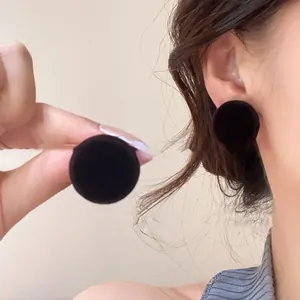 Detailed close-up showing black vintage circular fabric stud earrings on ear and fingers