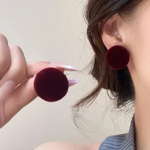 Detailed view of round burgundy velvet stud earrings shown on an ear for elegant style