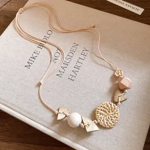 Bohemian woven rattan and wooden bead necklace displayed on an artistic book detail view.