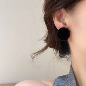 Detailed shot of black round fabric stud earrings worn on the ear for a vintage look