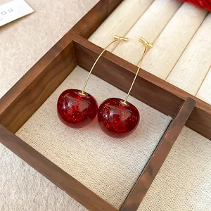 Detail of deep red cherry earrings with gold glitter inside a wooden box
