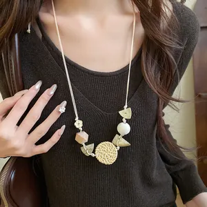 Close-up detail of a bohemian straw woven and wood bead necklace worn on a brown sweater.