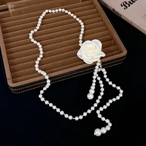 Vue détaillée d'un collier de perles élégant avec une grande rose en tissu blanc sur un plateau.