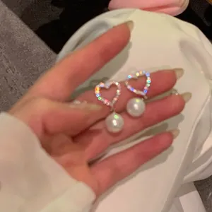 Détail rapproché d'élégantes boucles d'oreilles en cœur avec zircon et perle pendante.