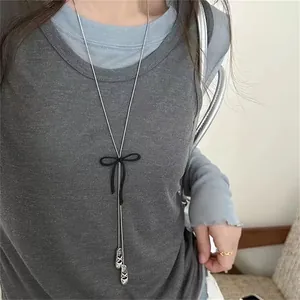 Detail view of a silver-tone long necklace featuring a black bow and ballet shoe pendants.