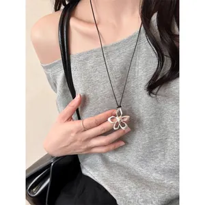 Silver flower pendant necklace worn with a grey ribbed top and black leather bag