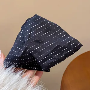 Vue détaillée d'une pince à cheveux en tissu noir avec des pois blancs mignons.