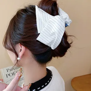 Vue détaillée d'une pince à cheveux en tissu blanc à pois noirs sur cheveux bruns