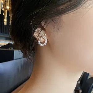 Gros plan de boucles d'oreilles couronne dorées avec nœud, perles et zircons sur l'oreille